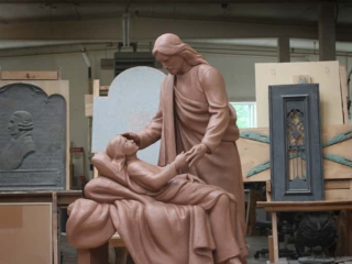 clay model of sculpture of Jesus Christ figure leaning over sick child on bed in sculpture studio