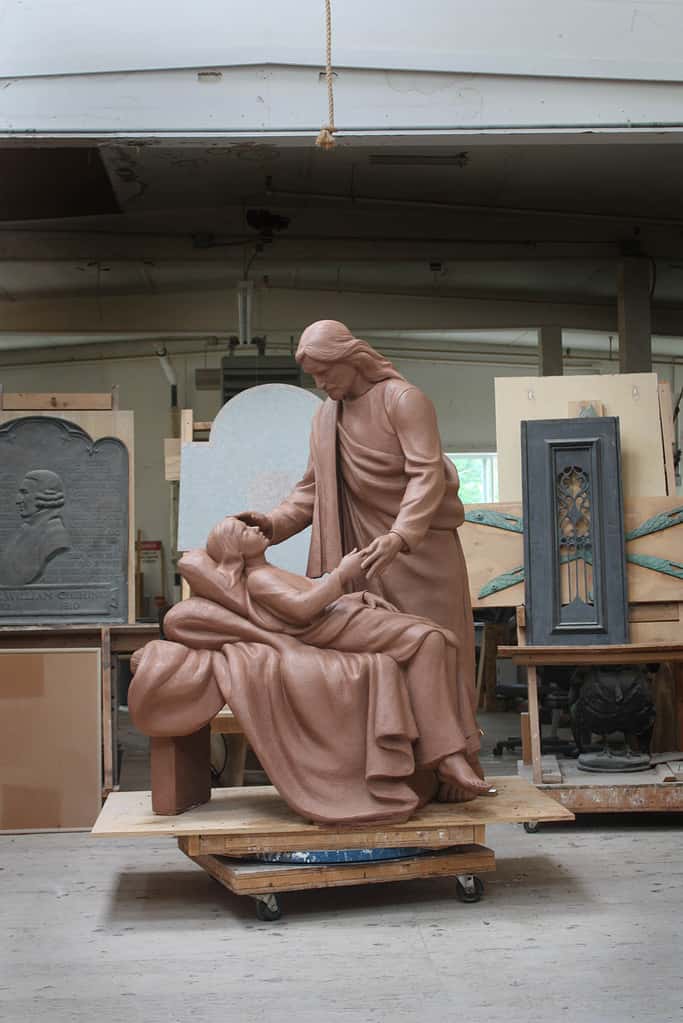 clay model of sculpture of Jesus Christ figure leaning over sick child on bed in sculpture studio