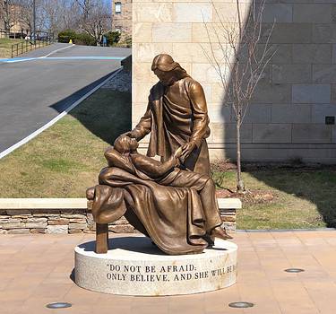 sculpture of two figures on round granite base on a walkway in front of a stone building