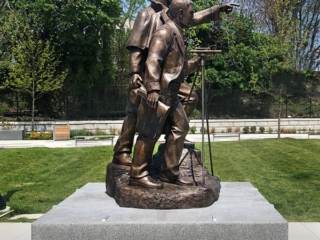 sculpture of two figures on square granite base in plaza with hardscaping and landscaping