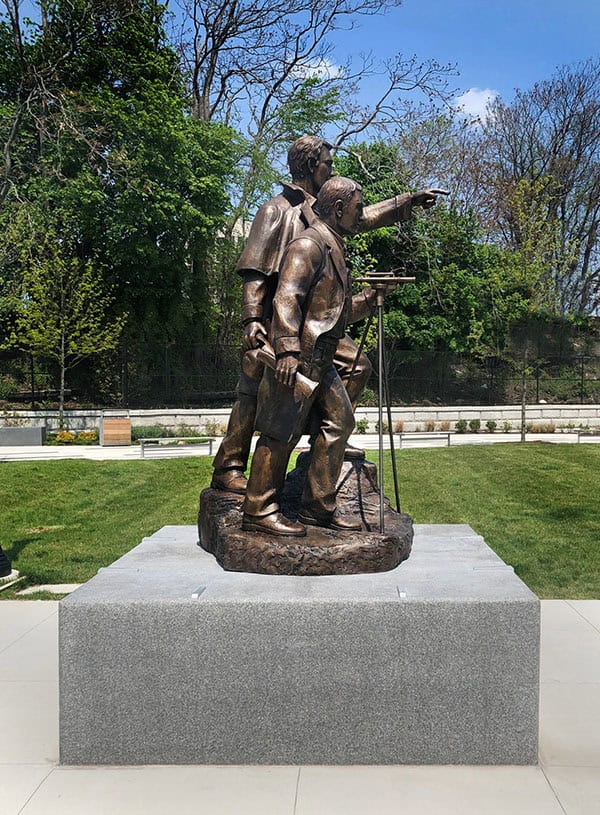 sculpture of two figures on square granite base in plaza with hardscaping and landscaping