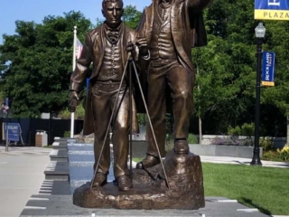sculpture of two figures on square granite base in plaza with hardscaping and landscaping