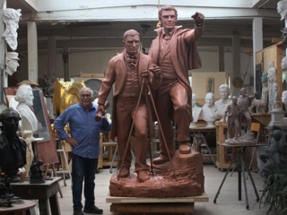 sculpture of two figures in studio with sculptor Robert Shure beside it