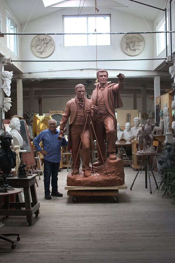 sculpture of two figures in studio with sculptor Robert Shure beside it